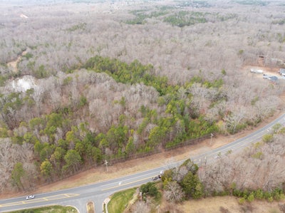 Aerial view of wooded land parcel along rural road with mixed evergreen and deciduous trees