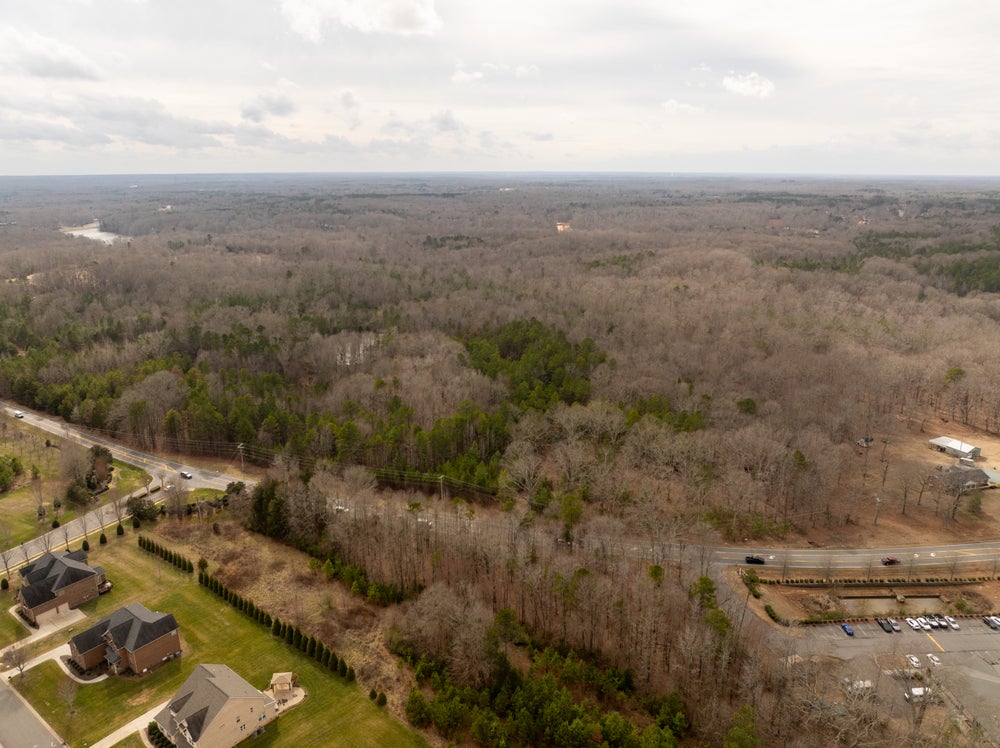 Aerial view of wooded land parcel with nearby residential homes and highway access