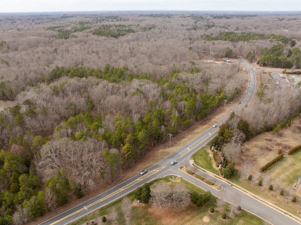 Aerial view of curved highway intersection surrounded by wooded land and sparse development