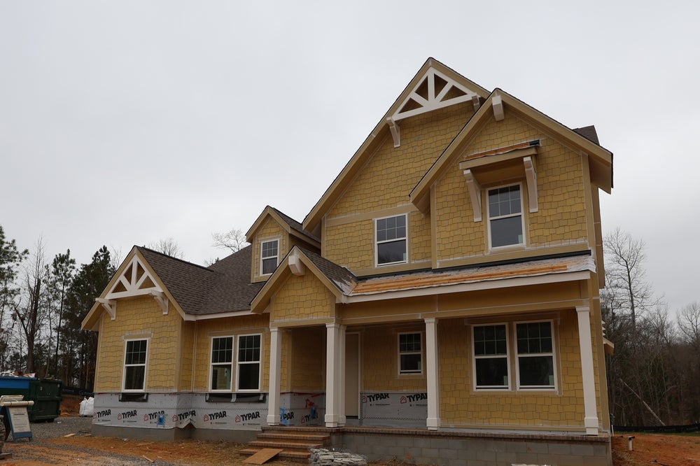 Two-story home under construction with yellow siding and decorative gable brackets