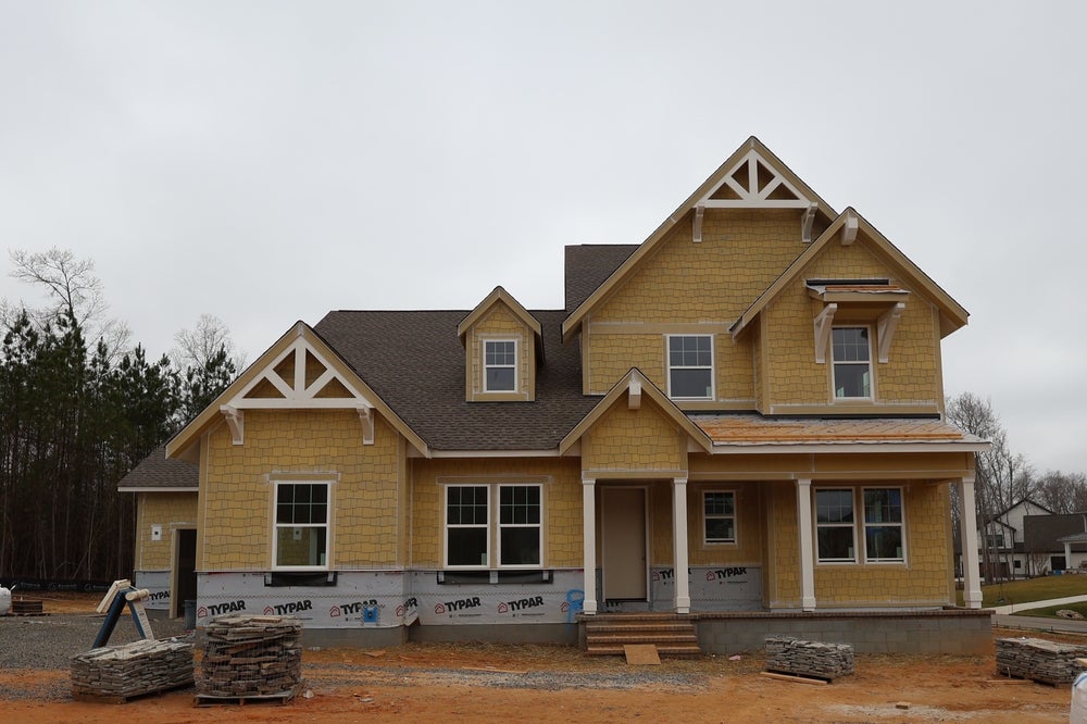 Two-story home under construction with yellow siding and craftsman-style gable details