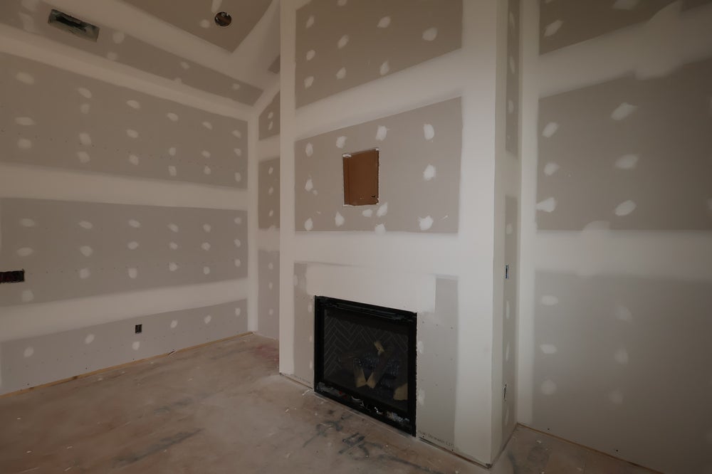 Living room under construction with fireplace and built-in shelving alcoves in unfinished drywall