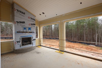 Covered porch under construction with fireplace and open walls overlooking wooded area