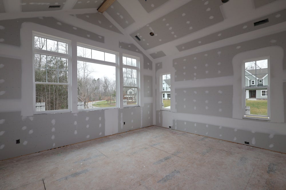 Empty room under construction with large windows and unfinished drywall walls