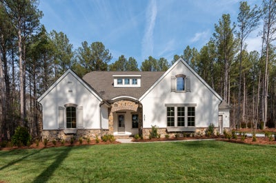 Single-story white stucco home with stone accents and arched entryway on wooded lot