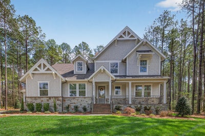 Two-story craftsman home with stone and shake siding, covered front porch, and wooded lot
