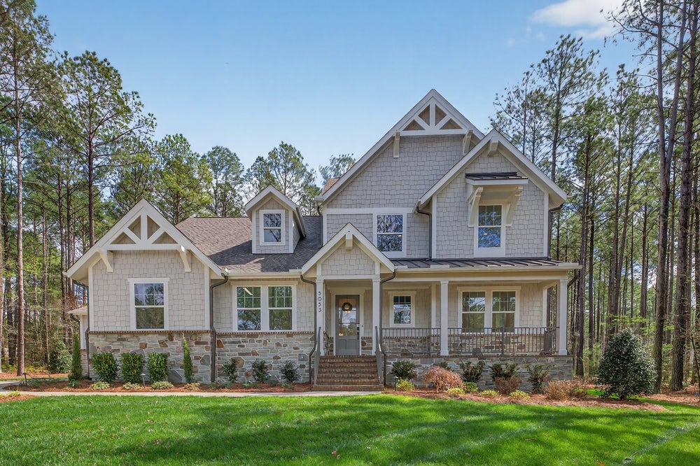 Two-story craftsman home with stone and shake siding, covered front porch, and wooded lot