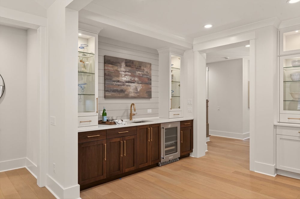 Wet bar with dark wood cabinets, glass shelving, and beverage cooler