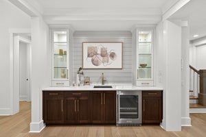 Wet bar with dark wood cabinets, white countertop, glass shelving, and beverage cooler