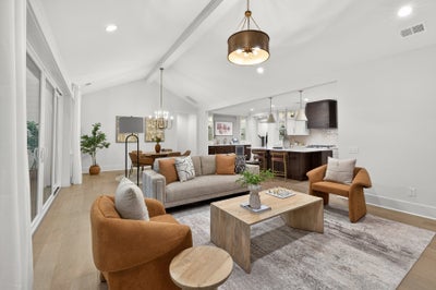 Open-concept living room and kitchen with vaulted ceiling, modern furniture, and bronze pendant light