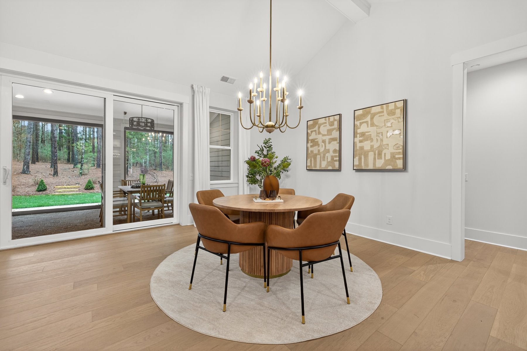 Dining room with round wood table, tan chairs, chandelier, and patio doors overlooking backyard