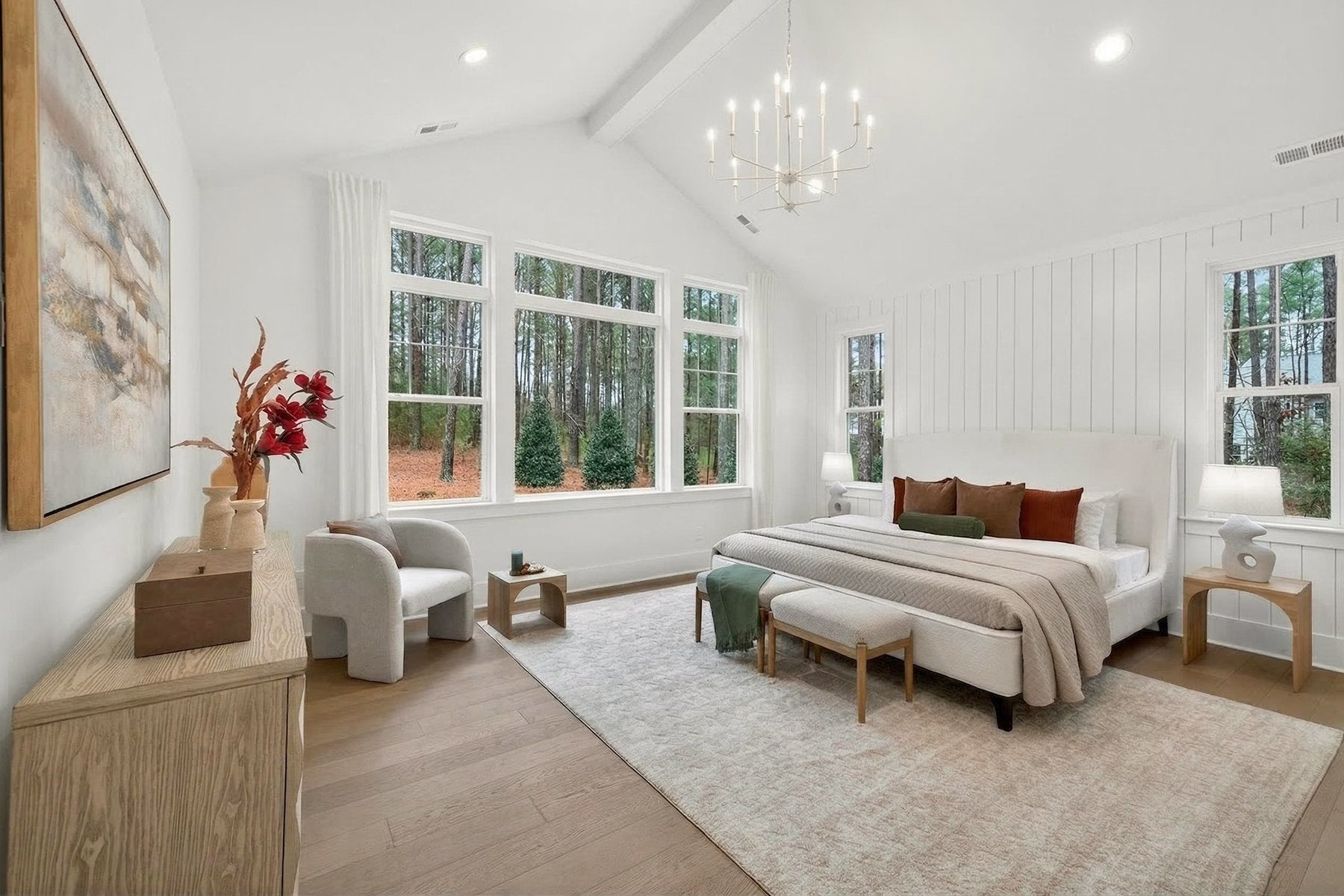 Master bedroom with vaulted ceiling, white shiplap walls, chandelier, and large windows overlooking woods
