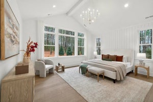 Master bedroom with vaulted ceiling, white shiplap walls, chandelier, and large windows overlooking woods
