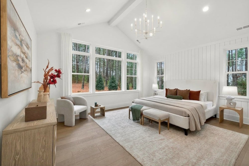 Master bedroom with vaulted ceiling, white shiplap walls, chandelier, and large windows overlooking woods
