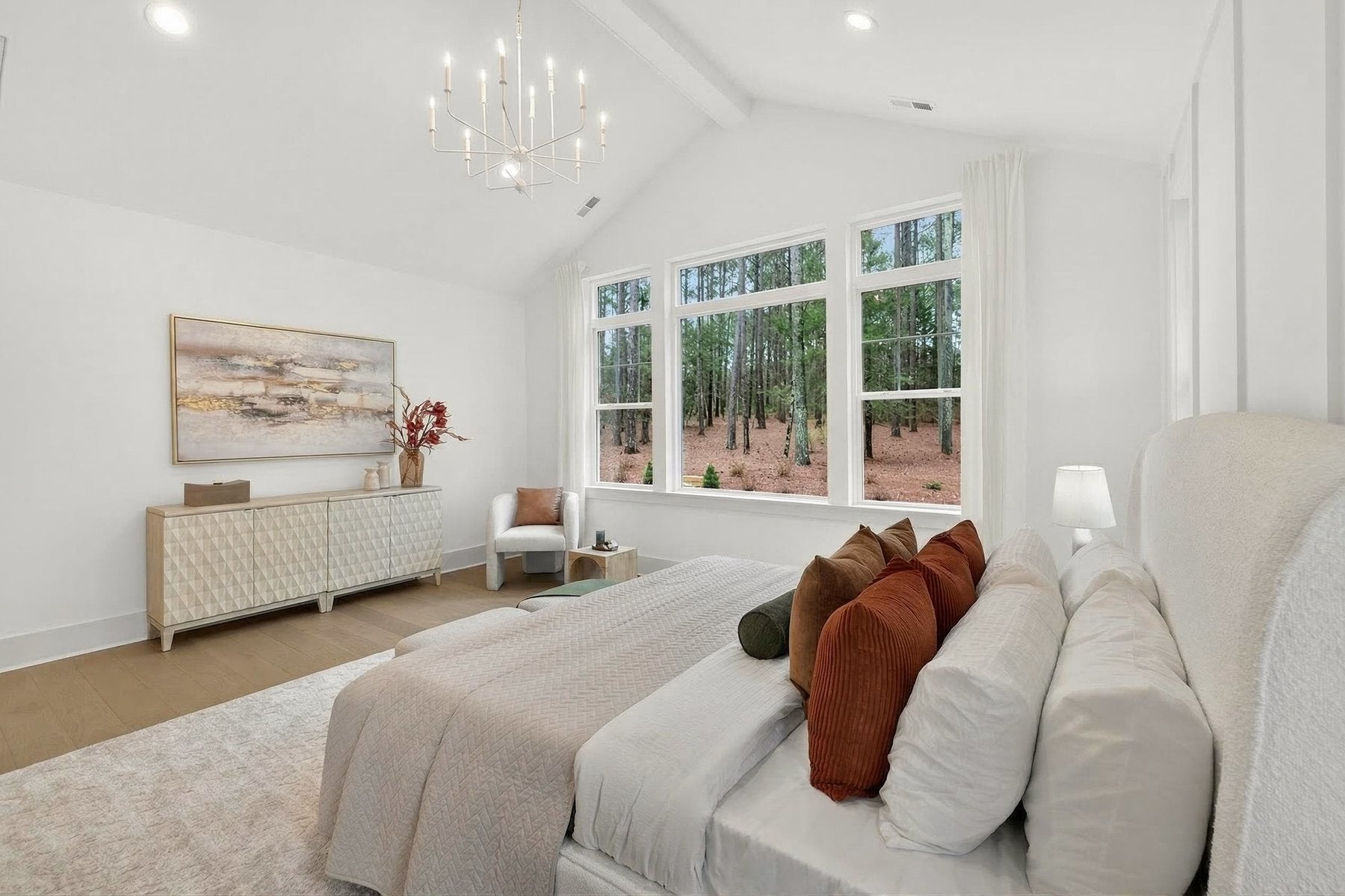 Master bedroom with vaulted ceiling, chandelier, and large windows overlooking wooded area