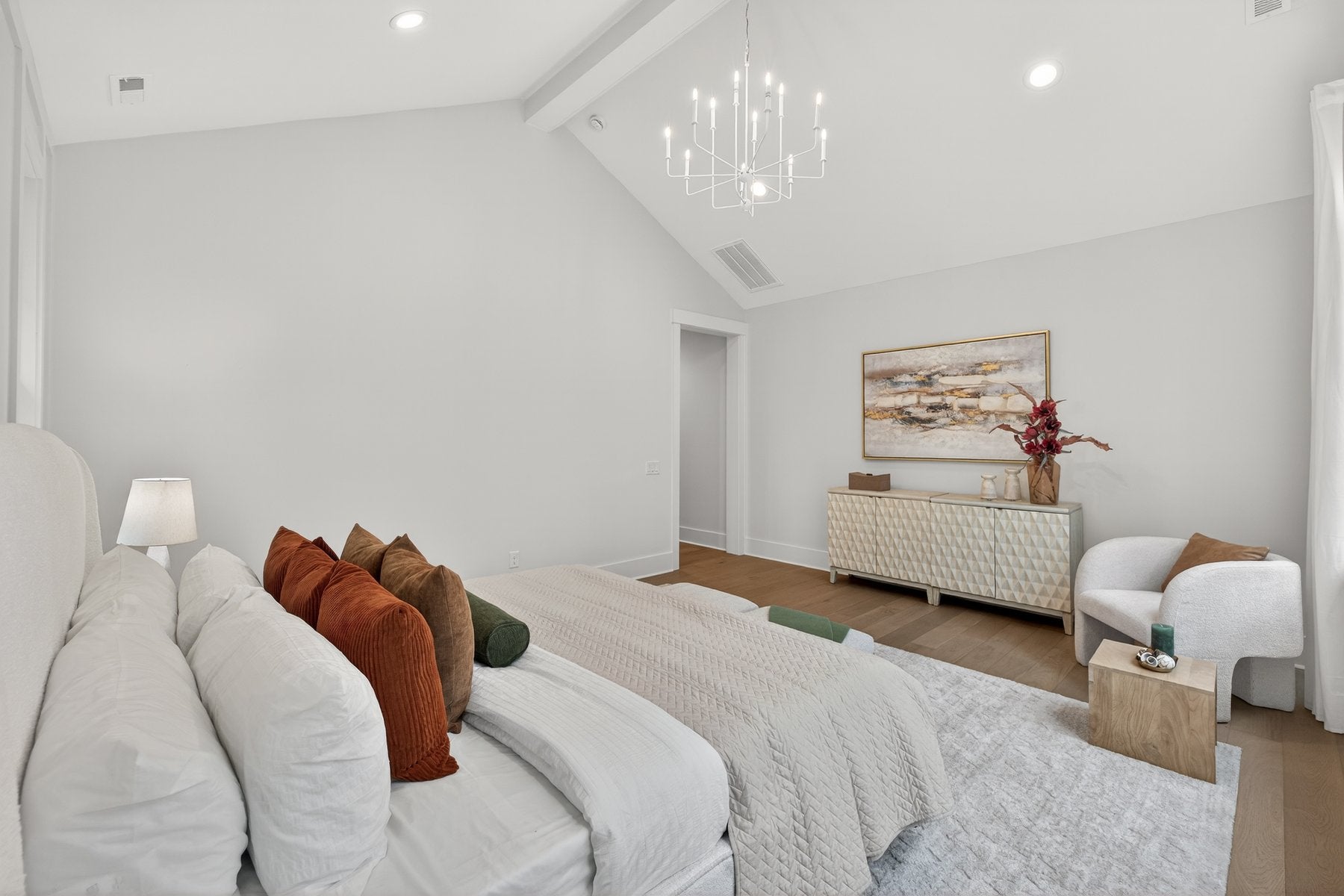 Spacious master bedroom with vaulted ceiling, chandelier, and white modern furnishings