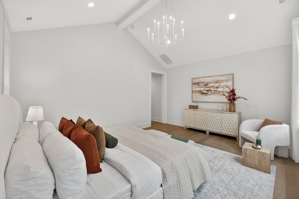 Spacious master bedroom with vaulted ceiling, chandelier, and white modern furnishings