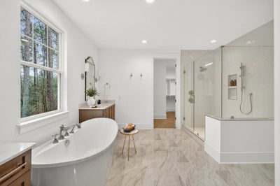 Modern master bathroom with freestanding tub, glass shower, and marble-look tile flooring