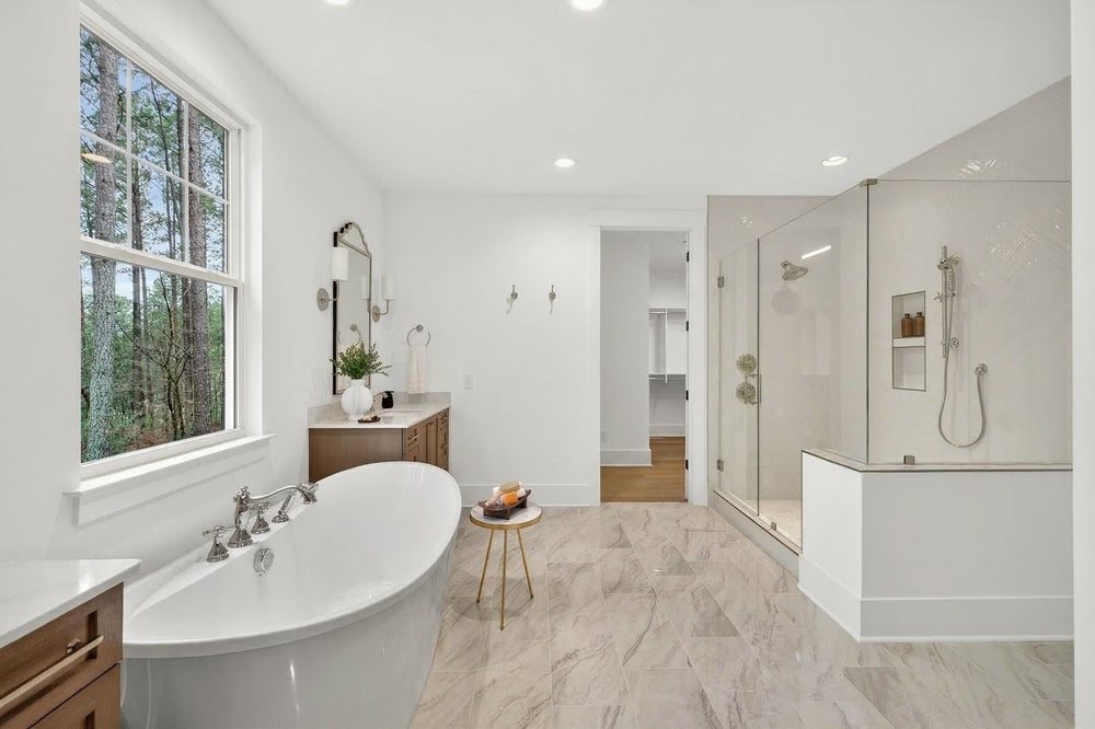 Modern master bathroom with freestanding tub, glass shower, and marble-look tile flooring