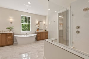 Master bathroom with freestanding tub, glass shower, wood vanities, and marble tile flooring