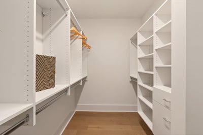 Walk-in closet with white built-in shelving, hanging rods, and hardwood flooring