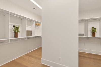 Walk-in closet with white built-in shelving, hanging rods, and hardwood floors