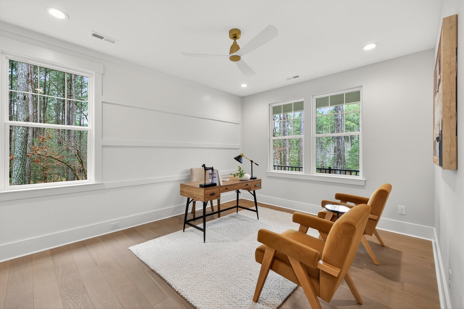 Home office with white shiplap walls, wood desk, and two orange accent chairs overlooking wooded view