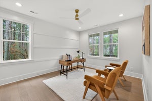Home office with white shiplap walls, wood desk, and two orange accent chairs overlooking wooded view