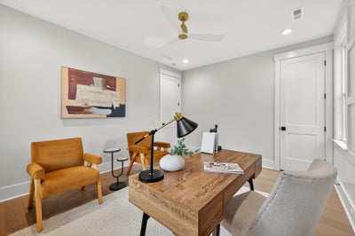 Home office with wood desk, orange accent chairs, and modern ceiling fan