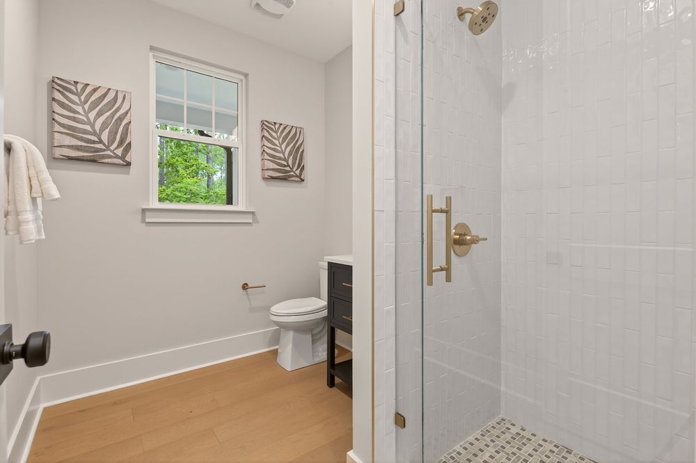 Modern bathroom with white subway tile shower, light wood floors, and gold fixtures