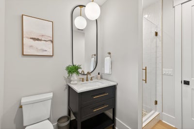 Modern bathroom with dark vanity, marble countertop, oval mirror, and glass shower enclosure with brass fixtures