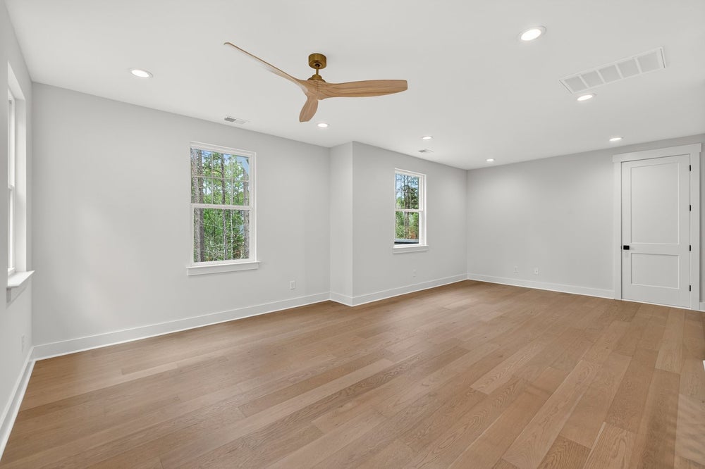 Empty room with light gray walls, hardwood floors, and ceiling fan