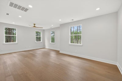 Empty room with light hardwood floors, white walls, and four windows with wooded views
