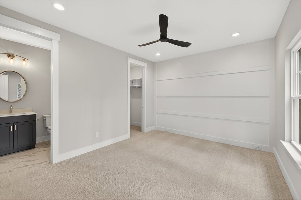 Empty bedroom with beige carpet, shiplap accent wall, and black ceiling fan