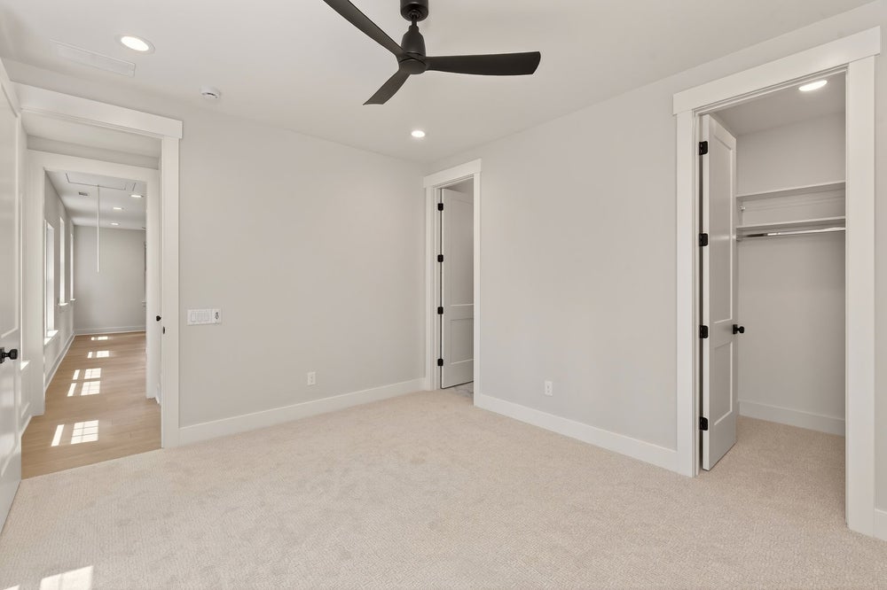 Empty bedroom with beige carpet, black ceiling fan, and walk-in closet