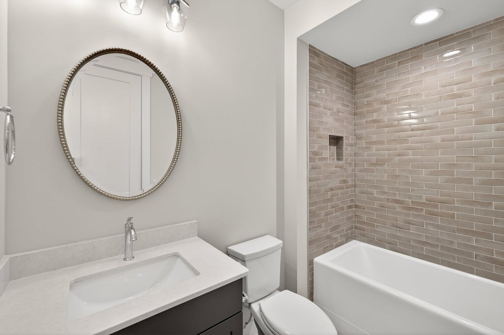 Modern bathroom with gray subway tile shower, round mirror, and white vanity