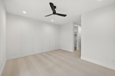Empty bedroom with white walls, beige carpet, and black ceiling fan