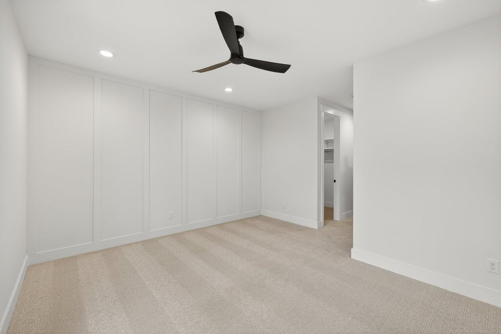 Empty bedroom with white walls, beige carpet, and black ceiling fan