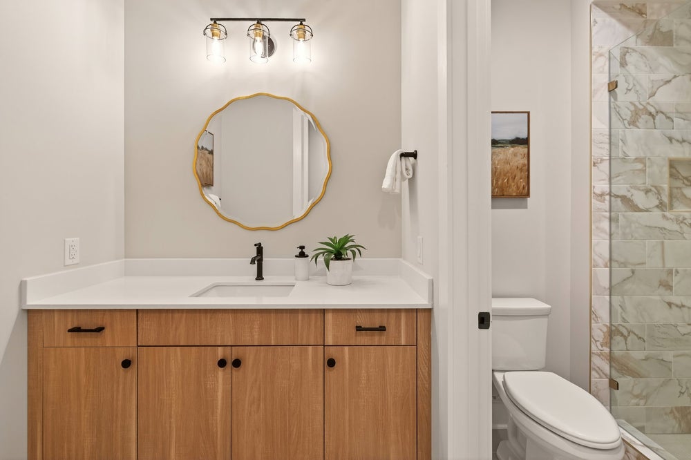 Bathroom with wood vanity, gold-framed mirror, and marble tile shower
