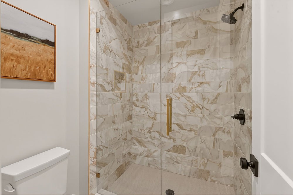 Walk-in shower with marble tile surround and glass door with brass hardware