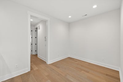 Empty room with light wood flooring, white walls, and recessed lighting with hallway view