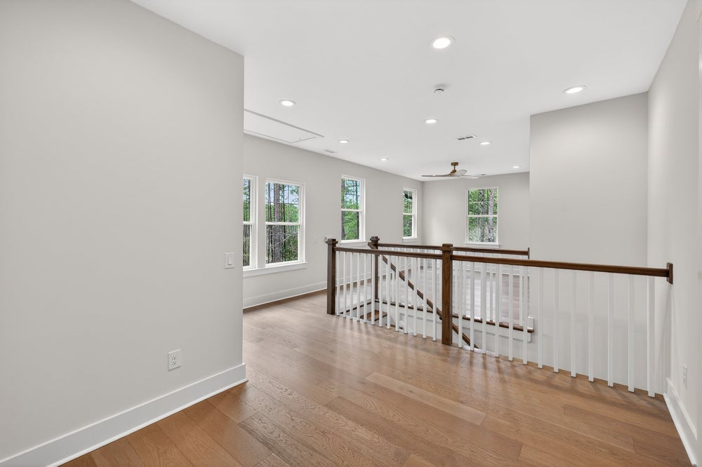 Upper floor landing with white railing, hardwood floors, and recessed lighting