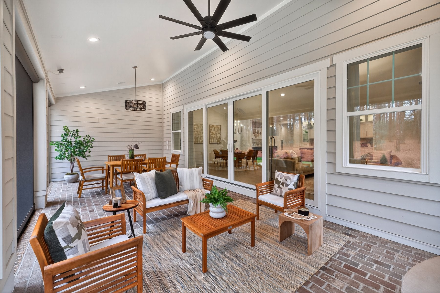 Covered patio with white shiplap walls, wooden furniture, ceiling fan, and sliding glass doors to interior