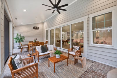 Covered patio with white shiplap walls, wooden furniture, ceiling fan, and sliding glass doors to interior