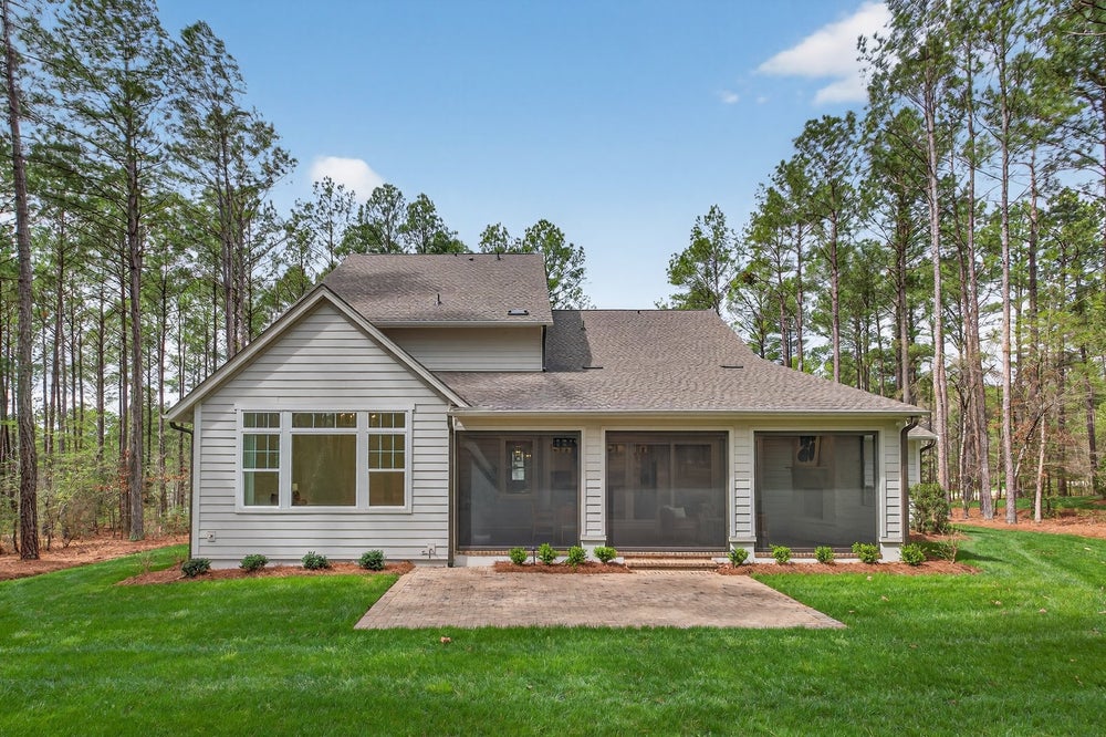 Single-story home with gray siding, three-car garage, and wooded lot