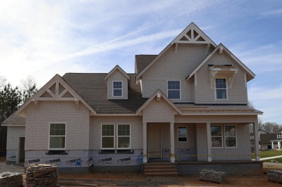 Two-story home under construction with beige brick exterior and decorative gable trim
