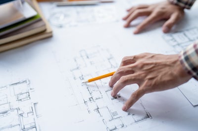 Hands reviewing architectural floor plans with pencil and material samples on desk