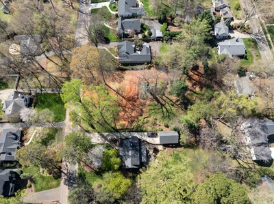 Aerial view of a vacant lot surrounded by mature trees in a residential neighborhood with nearby homes.