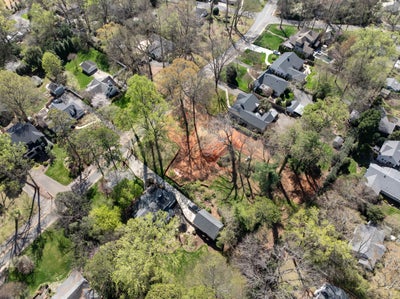 Aerial view of a vacant wooded lot surrounded by residential homes and tree-lined streets in a suburban neighborhood.