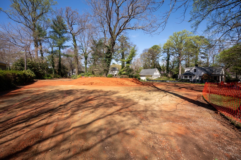Cleared residential lot with exposed red clay soil in established neighborhood